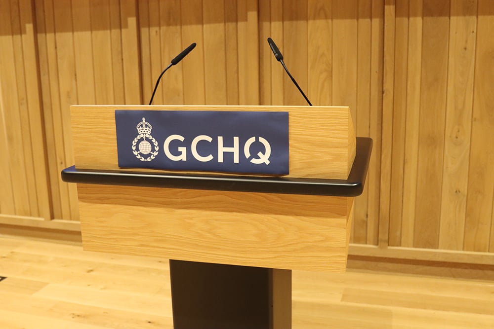 A lectern with a GCHQ logo on the front on a blue background