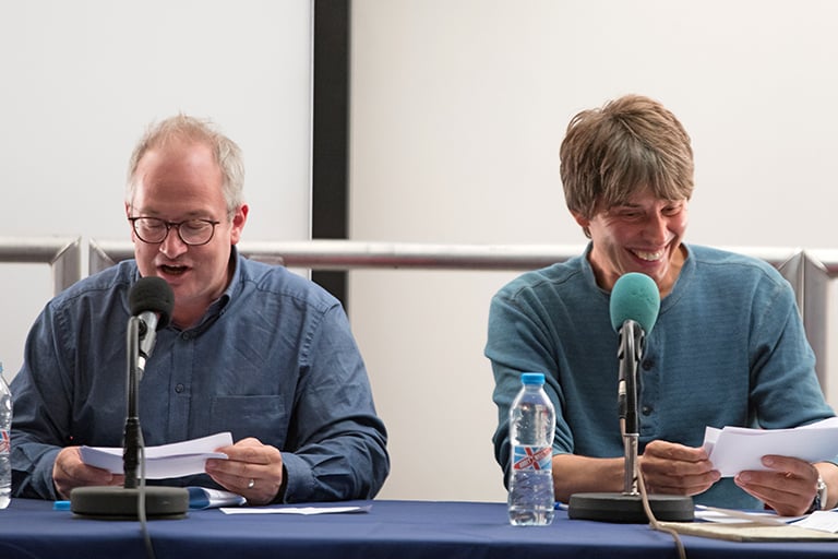 Both are reading notes. Robin is talking while Brian is laughing!