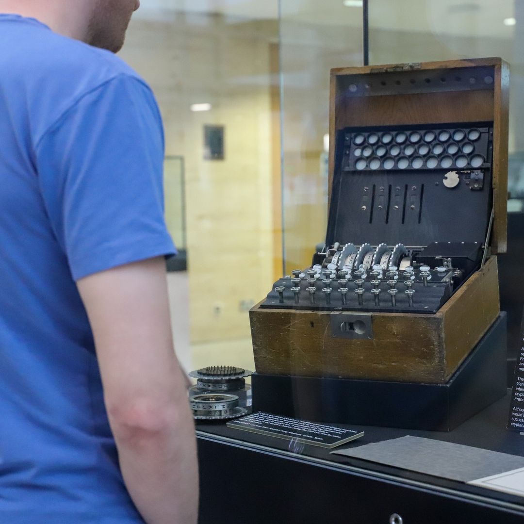 Robin has his back to camera as he looks at an Enigma machine within a glass display cabinet.