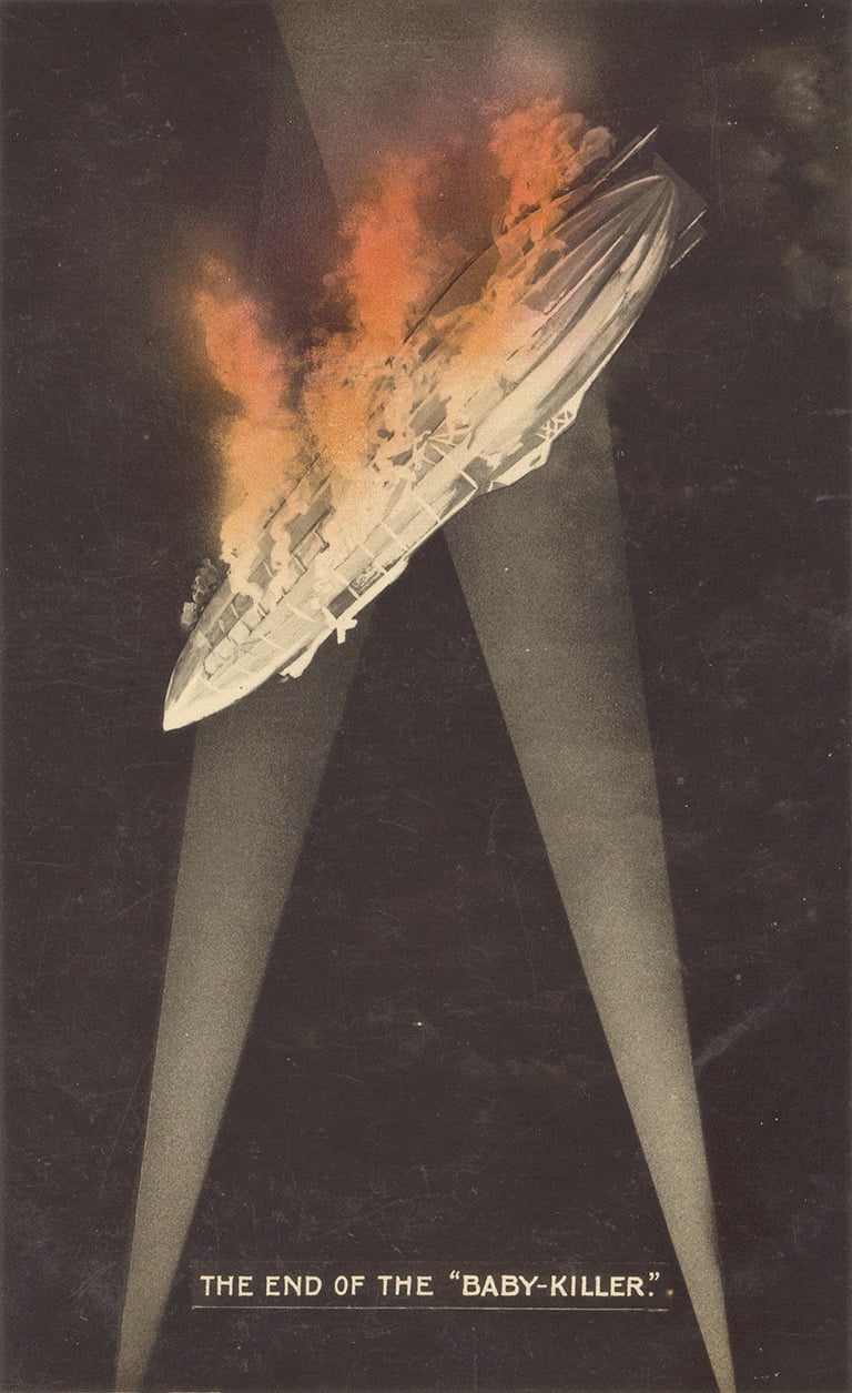 An illustration of a 'zeppelin' being shot down in flames, lit by searchlights.