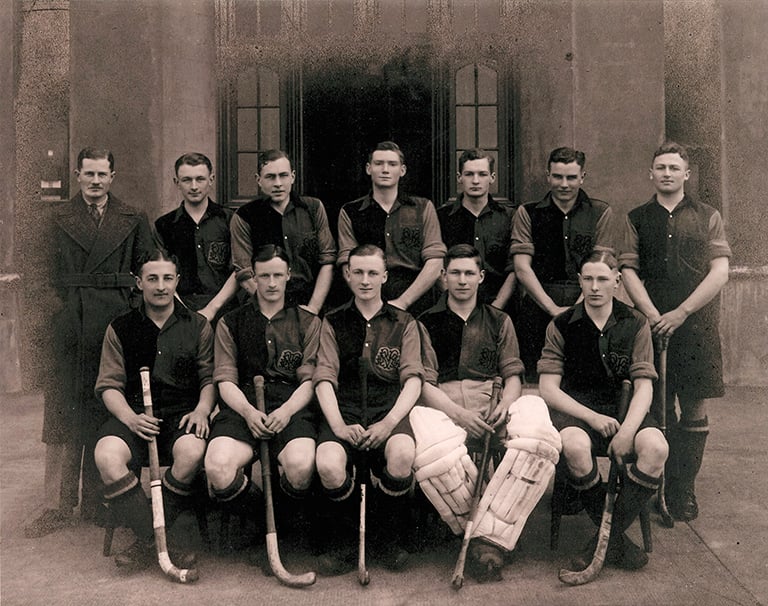 11 men in hockey outfits and their male coach in a trenchcoat