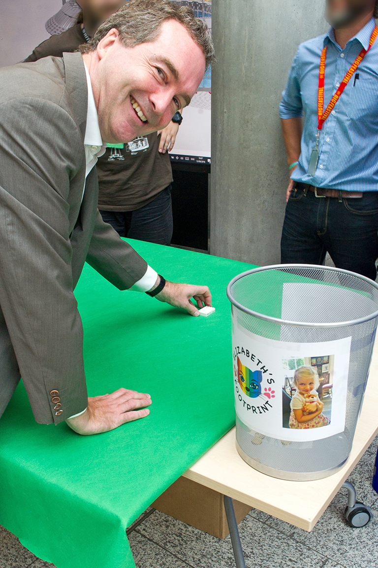 The Director places a small lego brick on a large table, by the Elizabeth's Footprint charity tin.