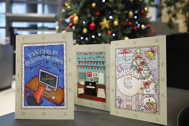 An image of a trio of Christmas Cards in the foreground. In the background is a Christmas tree.