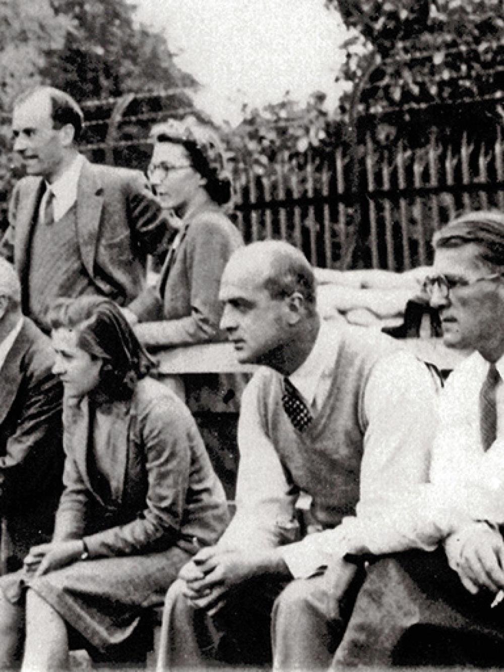 10 men, 2 women, in a group, watching something off camera to the left