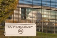 A 'no photography' sign on some fencing with a satellite dish in the background