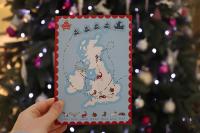 A hand holds the 2024 Christmas Card in front of a Christmas tree