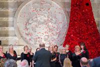 A choir sings in front of the GCHQ poppyfall in the atrium as poppies fall from the sky.