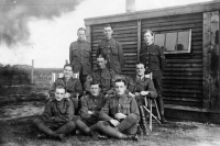 9 men in WWI uniform posing in front of a large shed and field