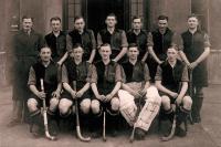 11 men in hockey outfits and their male coach in a trenchcoat