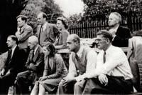 10 men, 2 women, in a group, watching something off camera to the left