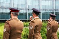 Three members of the armed forces blow whistles at the GCHQ War Memorial in the Benhall Courtyard